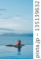 Relaxed man enjoying infinity pool with ocean view during tropical vacation 135139632