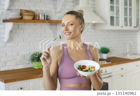 Happy woman eating a fresh salad bowl in bright kitchen for healthy living Happy woman eating a fresh salad bowl in bright kitchen for healthy living 135140962