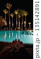 Couple relaxing by luxury pool at night with palm trees. 135142891
