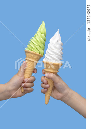 青い背景の前で二つの手が抹茶とバニラのソフトクリームコーンを持つ夏のスイーツ 135142971