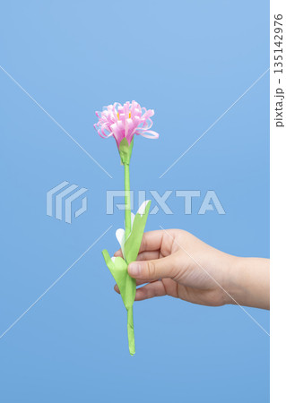 青背景に色紙と折り紙で作った花を持つ手 青背景に色紙と折り紙で作った花を持つ手 135142976
