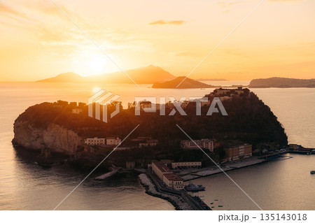 Sunset over Nisida with buildings on a hill and mountains in the distance. Naples, Italy Sunset over Nisida with buildings on a hill and mountains in the distance. Naples, Italy 135143018