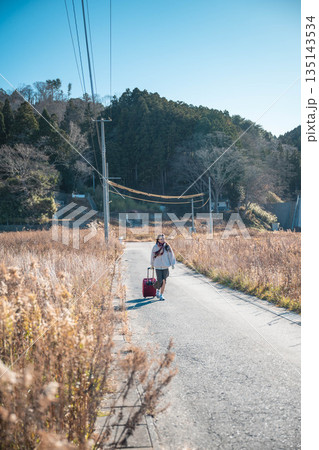 田舎道でキャリーバックを持っている若い女性 135143534