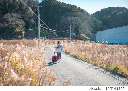 田舎道でキャリーバックを持っている若い女性 135143535
