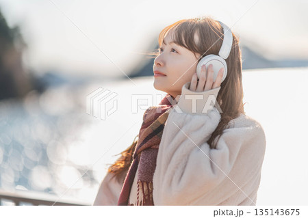 海辺に立ちヘッドホンで音楽を聴く若い女性 海辺に立ちヘッドホンで音楽を聴く若い女性 135143675