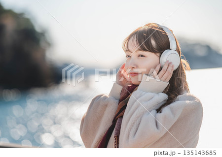 海辺に立ちヘッドホンで音楽を聴く若い女性 135143685