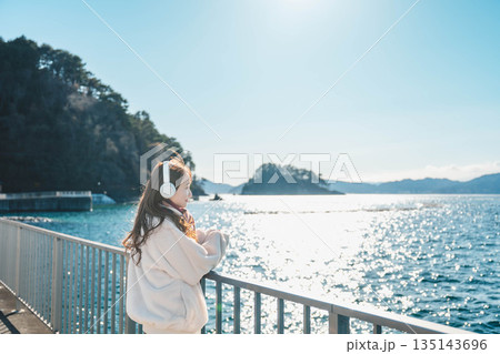 海辺に立ちヘッドホンで音楽を聴く若い女性 135143696