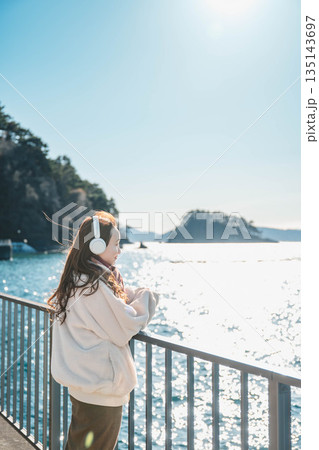 海辺に立ちヘッドホンで音楽を聴く若い女性 135143697