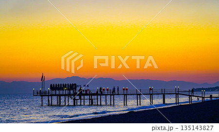 Serene Sunset Over a Peaceful Pier with Silhouetted Figures Against a Colorful Sky Reflecting on Calm Waters Serene Sunset Over a Peaceful Pier with Silhouetted Figures Against a Colorful Sky Reflecting on Calm Waters 135143827