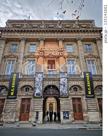 Paris, France - December 10, 2025: The grand entrance of the Monnaie de Paris (Paris Mint). The neoclassical facade features tall columns, intricate stone carvings, and a copper-colored circular sign 135143881