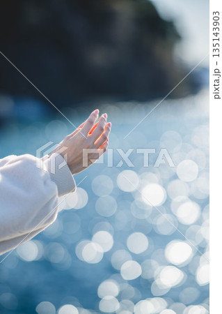 海辺に立つ女性の手元 135143903