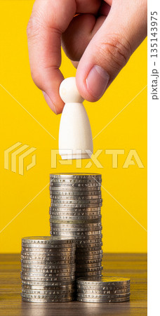 Hand placing person figure on coin stacks 135143975