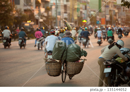 Evening rush hour with motorcycle riders in Asian city, soft focus on bicycle with two baskets. 135144052
