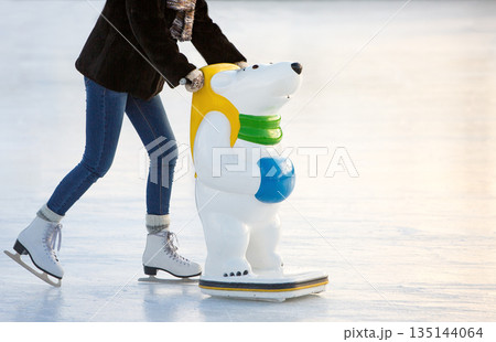 Skater helpers to keeps balance on ice. Woman ion figure skates with learning figure on ice rink 135144064