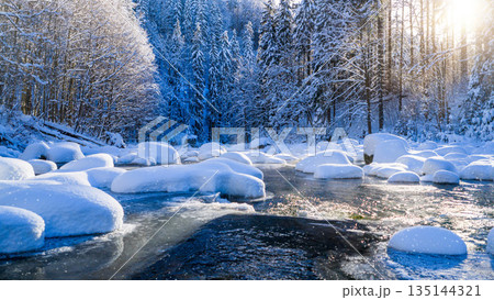 Peaceful winter river flowing through a snow covered forest during gentle snowfall. Soft sunlight reflects on icy water, creating a calm, atmospheric, and serene winter nature scene. Peaceful winter river flowing through a snow covered forest during gentle snowfall. Soft sunlight reflects on icy water, creating a calm, atmospheric, and serene winter nature scene. 135144321