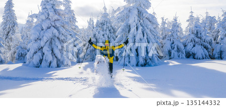 Happy young man celebrating in a snowy winter landscape while snowshoe hiking. Joyful moment in a frost covered forest, expressing freedom, energy, and connection with nature. 135144332