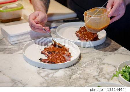Chef preparing dishes with sauce at a modern kitchen Chef preparing dishes with sauce at a modern kitchen 135144444