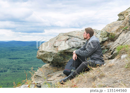 A man in a gray jacket is sitting on a mountain top. A man in a gray jacket is sitting on a mountain top. 135144560