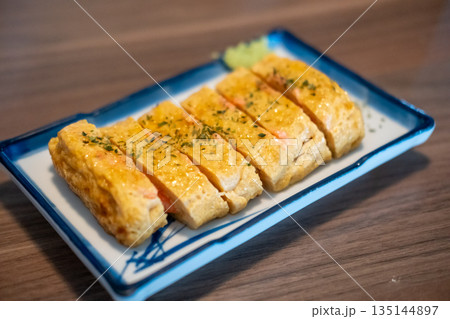 Tamagoyaki, a Japanese omelette made by rolling together several layers of fried beaten eggs, served on a plate. Tamagoyaki, a Japanese omelette made by rolling together several layers of fried beaten eggs, served on a plate. 135144897