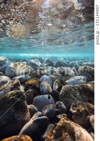 Underwater landscape with stones sea bottom and sun rays in water. 135144997