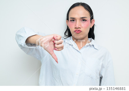 Portrait of a young Thai transgender person with thumbs down gesture against white background Portrait of a young Thai transgender person with thumbs down gesture against white background 135146881