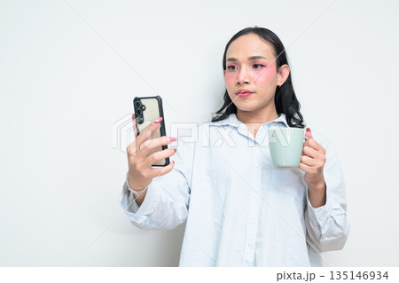 Portrait of Thai transgender person using phone and holding coffee cup against white background Portrait of Thai transgender person using phone and holding coffee cup against white background 135146934