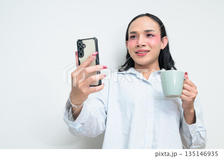 Portrait of Thai transgender person using phone and holding coffee cup against white background 135146935