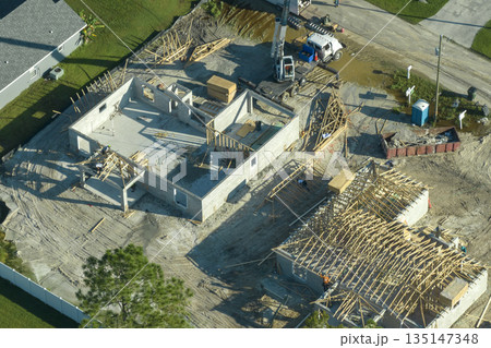Builders working on roof construction of unfinished residential house with wooden frame structure in Florida suburban area. Housing development concept Builders working on roof construction of unfinished residential house with wooden frame structure in Florida suburban area. Housing development concept 135147348