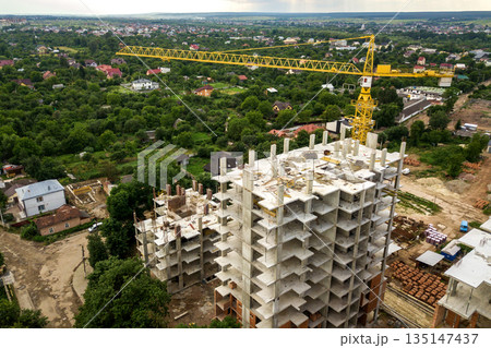 Aerial view of tower lifting crane and concrete frame of tall apartment residential buildings under construction in a city. Urban development and real estate growth concept. 135147437