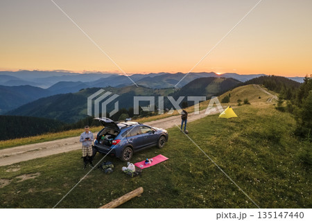 Aerial view of tourist camping tents and off road car on mountain campsite at bright sunny evening. Active tourism and offroad driving adventure concept Aerial view of tourist camping tents and off road car on mountain campsite at bright sunny evening. Active tourism and offroad driving adventure concept 135147440