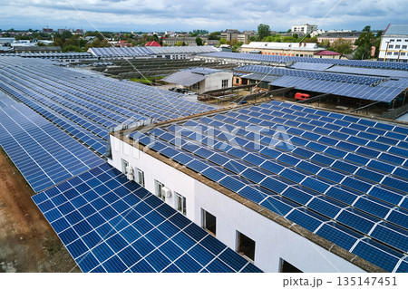 Aerial view of solar power plant with blue photovoltaic panels mounted on industrial building roof for producing green ecological electricity. Production of sustainable energy concept. 135147451