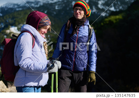 Two Friends Hiking In Winter Gear On Mountain Trail With Backpacks 135147635