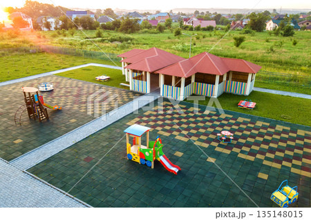 Aerial view of new alcove in kindergarten play yard with red tiled roof for outdoor children activities. Aerial view of new alcove in kindergarten play yard with red tiled roof for outdoor children activities. 135148015