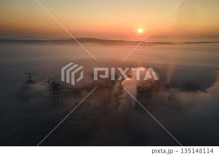 Aerial view of cement factory with high concrete plant structure and tower crane at industrial manufacturing site on foggy evening. Production and global industry concept. Aerial view of cement factory with high concrete plant structure and tower crane at industrial manufacturing site on foggy evening. Production and global industry concept. 135148114