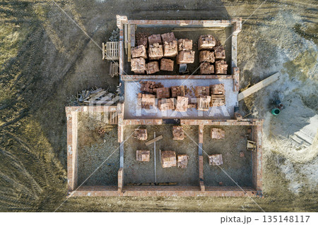Aerial view of building site. Trenches dug in ground and filled with cement as foundation for future house, brick basement floor and stacks of brick for construction. 135148117