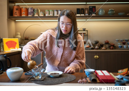 Woman Pouring Tea From A Teapot Into A Teacup At A Table Woman Pouring Tea From A Teapot Into A Teacup At A Table 135148323