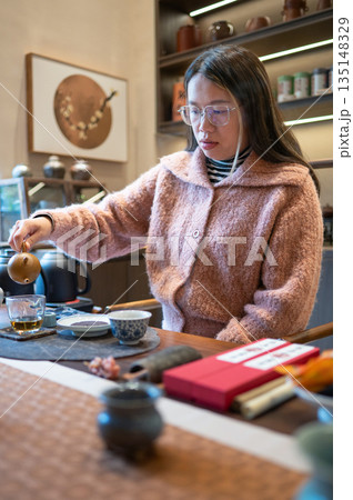 Female Tea Master Pouring Tea From A Teapot Into A Teacup At A Table 135148329