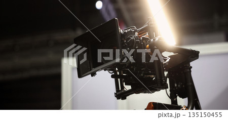 Behind the scenes of movie shooting or filming or video production with high quality camera and tripod equipment set up and professional film crew team in studio lighting. Video production camera gear Behind the scenes of movie shooting or filming or video production with high quality camera and tripod equipment set up and professional film crew team in studio lighting. Video production camera gear 135150455