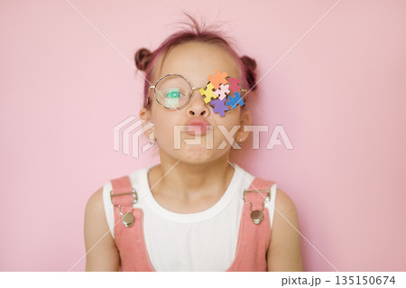 A child with a decorated lens made of stickers of multicolored puzzle pieces blows a kiss. World Autism Awareness Day 135150674