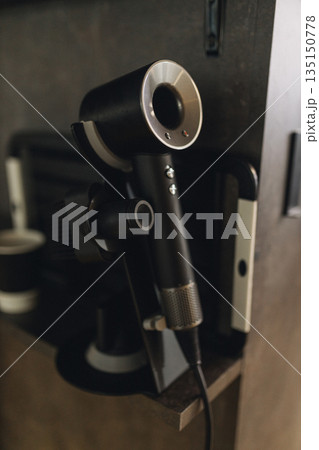 Professional hair dryer hanging on wall in barbershop. Modern grooming equipment, barber salon interior detail, hairstyling tool, clean minimal workplace concept. 135150778