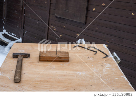 Hammer, nail and metal hooks arranged on a wooden workbench outdoors in winter. Construction and repair concept in cold snowy conditions. Hammer, nail and metal hooks arranged on a wooden workbench outdoors in winter. Construction and repair concept in cold snowy conditions. 135150992
