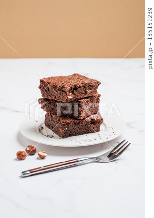 Chocolate brownie on a plate on a marble background with nuts and fork. 135151239
