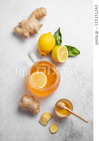 Flat lay of a glass cup of hot tea with fresh lemon and ginger on a light textured background 135151243