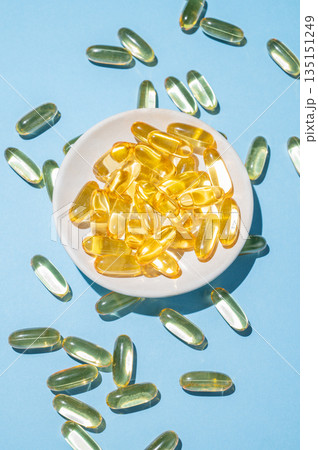 Yellow softgel vitamins capsules on a plate on a blue background. Yellow softgel vitamins capsules on a plate on a blue background. 135151249
