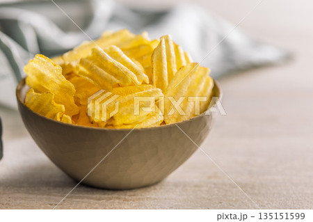 Wavy potato chips in bowl on kitchen table. 135151599