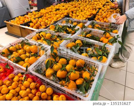 A man selects ripe, bright orange tangerines with green leaves. A woman fills a bag with produce from a large grocery store display, emphasizing the importance of healthy eating and fresh fruit. A man selects ripe, bright orange tangerines with green leaves. A woman fills a bag with produce from a large grocery store display, emphasizing the importance of healthy eating and fresh fruit. 135151627