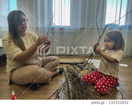 Mother and daughter enjoy creative bonding making an art project from natural twigs on the floor, fostering creativity and education through handmade crafts in a domestic setting. Mother and daughter enjoy creative bonding making an art project from natural twigs on the floor, fostering creativity and education through handmade crafts in a domestic setting. 135151632