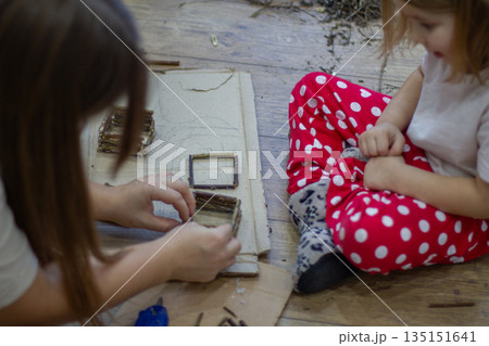 Mother and child creating a miniature house using twigs and natural materials, fostering creativity, education, and family bonding through diy craft activities. Mother and child creating a miniature house using twigs and natural materials, fostering creativity, education, and family bonding through diy craft activities. 135151641