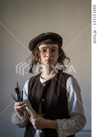 Freelance artist with calm concentrated glance holding canvas, paint brushes, looking at camera 135151668