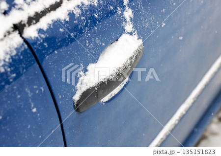Closeup image of car door handle covered in snow with icy edges and textured surface 135151823
